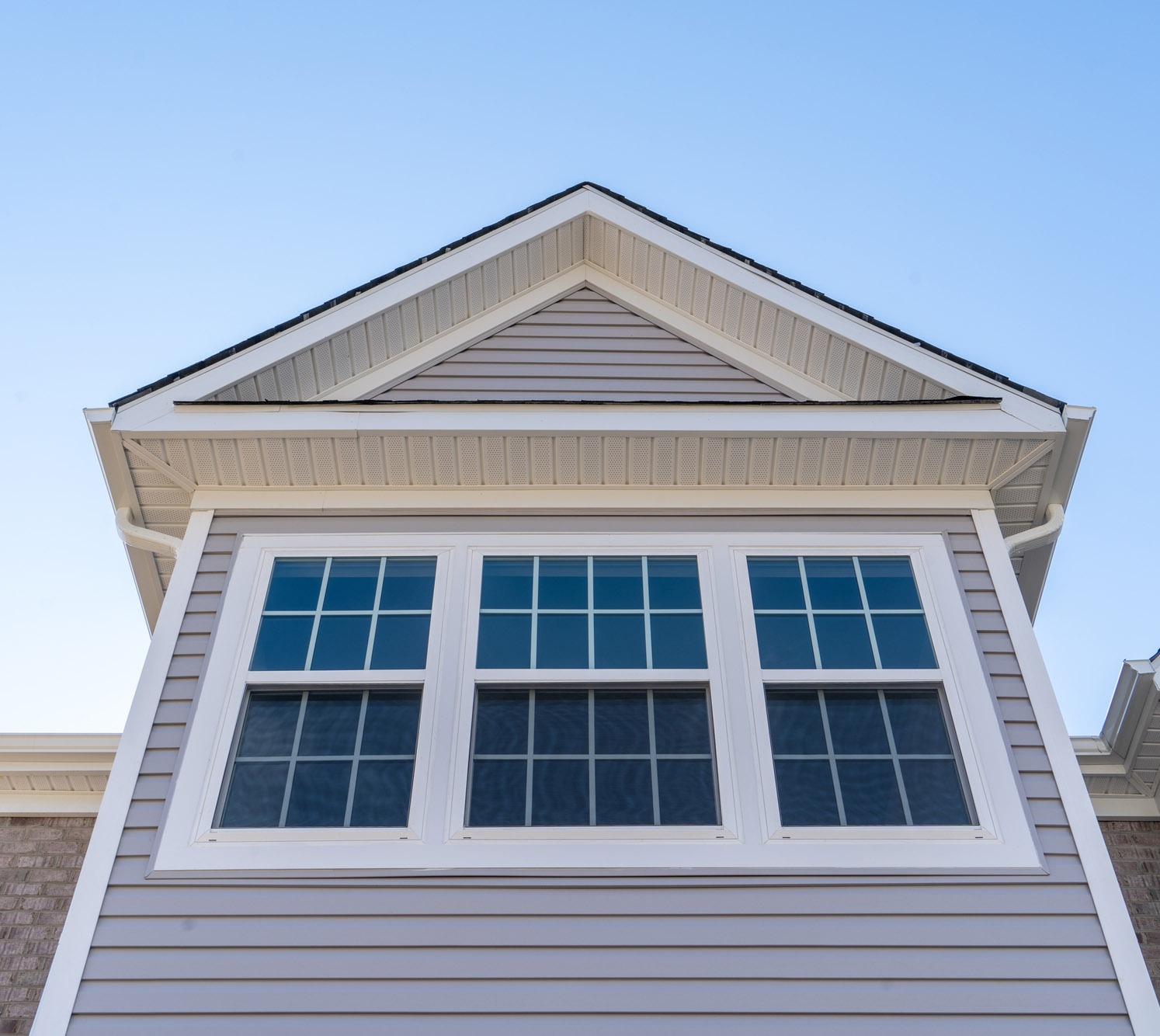 Stylish house exterior featuring a gabled roof and large multi-pane windows against a clear blue sky, highlighting residential architecture.